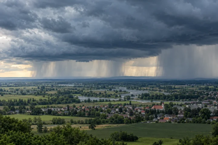 Ciemne chmury burzowe i kilka kurtyn deszczu nad polami oraz niewielkim miastem
